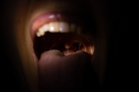 Open mouth of a girl in the dark with a beam of light in the mouth with visible tongue and teeth, wide open mouthの写真素材