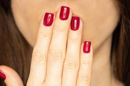 Woman's hand with red manicure covers lips, gesture of silence or secret
