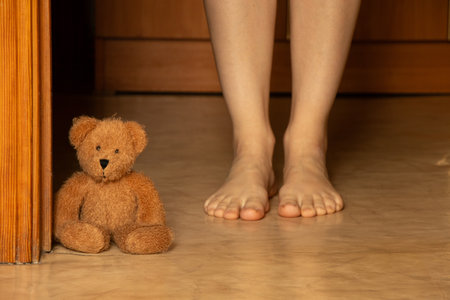 Teddy bear at the door and bare feet on the floor in the apartment, children's comfort at home, familyの写真素材