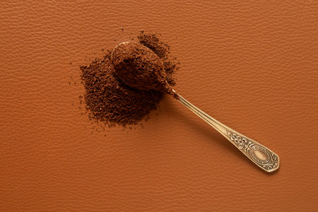 Spoon with ground coffee beans on brown leather background, aromatic morning drinkの写真素材