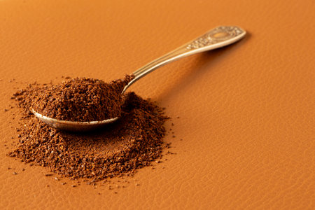 Spoon with ground coffee beans on brown leather background, aromatic morning drinkの写真素材