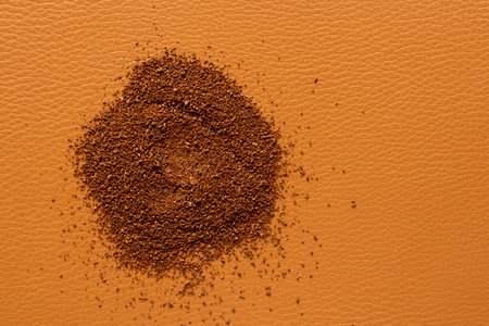 Scattered ground coffee beans on a brown leather background close-upの写真素材