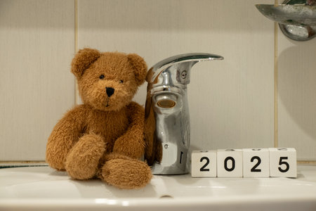 Brown soft baby teddy bear sits on the sink in the bathroom and next to it are cubes with the year 2025, bathroomの写真素材