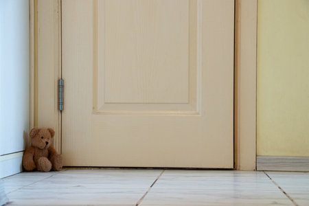 Brown baby teddy bear sits in the corner by the door in the apartment on the floor, baby toyの写真素材