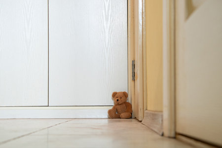 Brown baby teddy bear sits in the corner by the door in the apartment on the floor, baby toyの写真素材