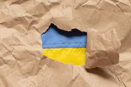 Flag of Ukraine seen through torn craft paper as symbolism, freedom, patriotismの写真素材