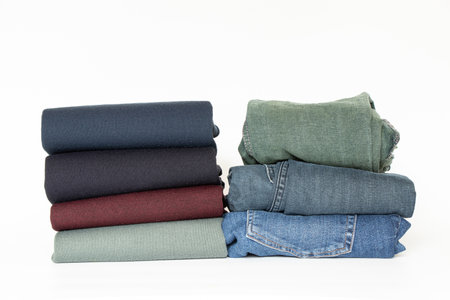Folded men's sweaters and jeans on a white background, a set of clothes for a wardrobe, store or advertisingの写真素材
