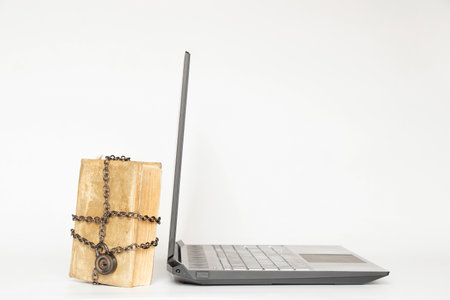 Old book in chains next to modern laptop on white background, secret knowledgeの写真素材