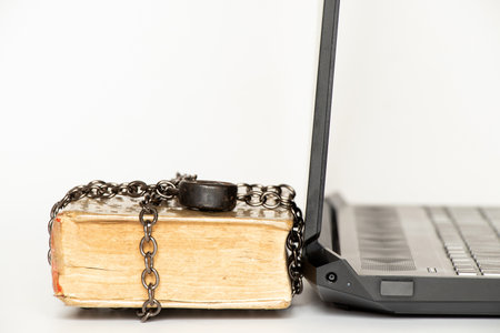 Old book in chains next to modern laptop on white backgroundの写真素材