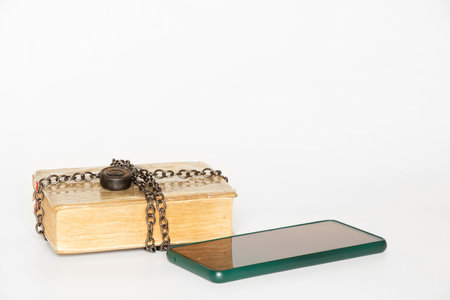 Old book in chains and smartphone on white backgroundの写真素材