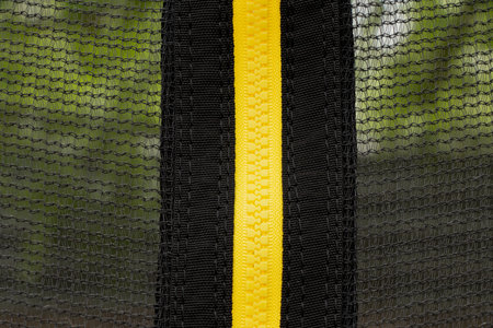 Yellow plastic zipper vertical on black mesh, close-up of fastener on textile background for design or fashion projectsの写真素材