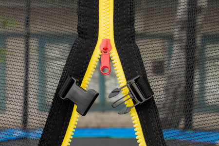 Yellow zipper with red puller and black plastic fastener on mesh background, close-up of textile...