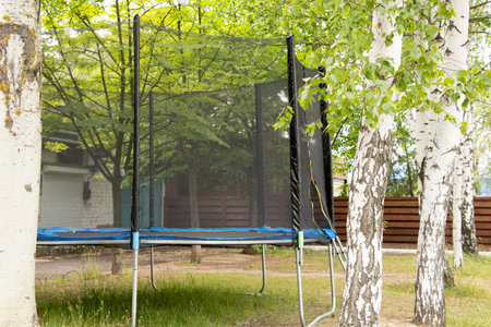Trampoline with safety net in the park among trees in summer, active outdoor recreationの写真素材