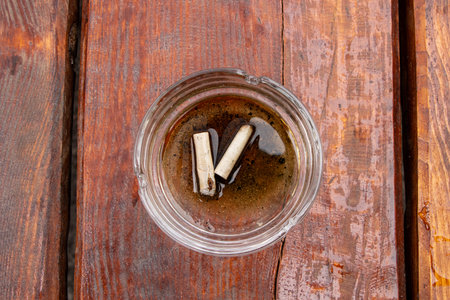 Cigarette butts in a glass ashtray in water on a wooden surface, bad habit, smoking and nicotine addictionの写真素材