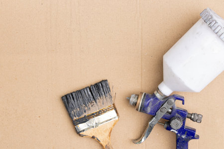 Spray gun and used brush with black paint on cardboard, tools for repair, restoration and finishing worksの写真素材