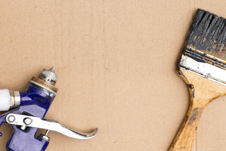 Spray gun and used brush with black paint on cardboard, tools for repair, restoration and finishing worksの写真素材