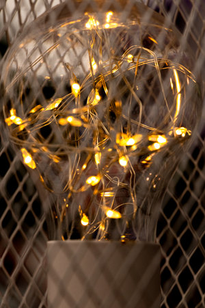 Garland inside a light bulb on a metal mesh background, warm light, decoration, cozy interiorの写真素材