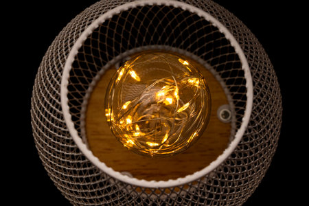 Garland inside a light bulb on a metal mesh background, warm light, decoration, cozy interiorの写真素材