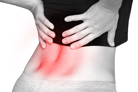 Young girl holding her back because of back pain, sitting on a white background, acute back painの写真素材