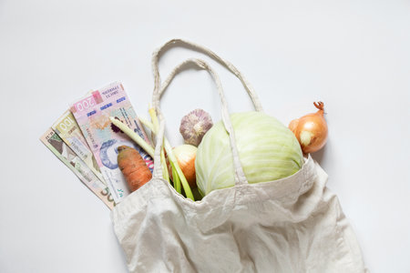 Vegetables in an eco-bag with Ukrainian hryvnia, grocery shopping, food and vegetable prices in Ukraine, inflation and food costsの写真素材