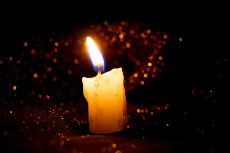 Burning candle on golden glitter background and bokeh on black background, candle flameの写真素材