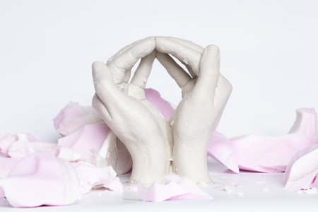 Plaster sculpture of clasped hands on white background among pink gel remnants of hand mold, plaster handsの写真素材
