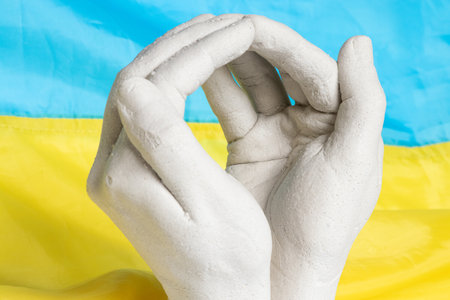 Plaster sculpture of clasped hands against the background of the Ukrainian flagの写真素材
