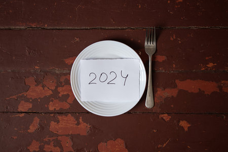 2024 written on piece of paper in plate with fork on red wooden surfaceの写真素材
