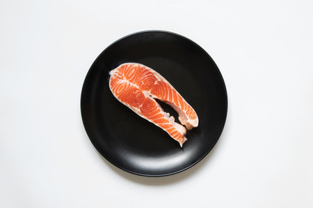 A piece of raw salmon lies in a black plate on a white background close-upの写真素材