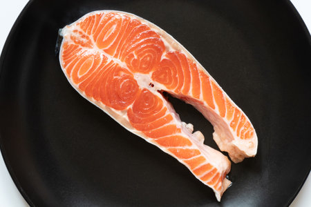 A piece of raw salmon lies in a black plate close-upの写真素材
