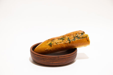 Piece of aromatic garlic bread with herbs bitten in wooden plate on white backgroundの写真素材