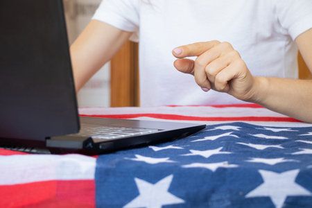 Girl working on laptop on table with American flag, freelance, online work from homeの写真素材