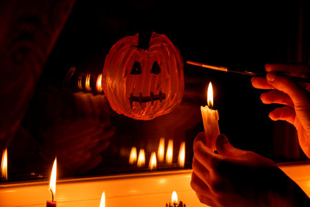 A girl draws a pumpkin for Halloween on the window in an apartment by candlelight, decor for the Halloween holidayの写真素材