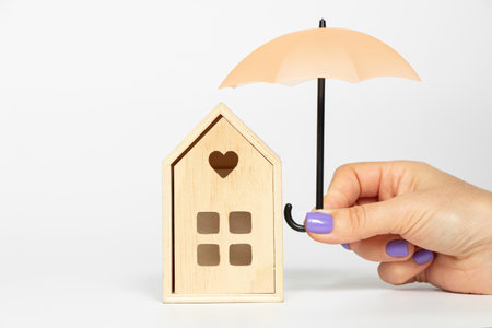 Miniature wooden house under umbrella in girl's hand on white background, weather, home and comfortの写真素材