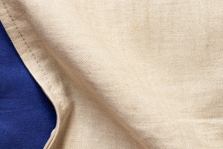 Natural beige linen fabric texture as a background for design and creativity with a bend and part of the blue fabric underneath, fabric backgroundの写真素材