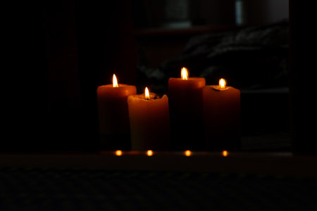 Two burning candles stand on chairs near a mirror and in the reflection of the mirror candles are visible in a room in the dark, candle flameの写真素材