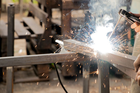 Welding metal parts with sparks and smoke - the work process of a welder joining metal elements with...