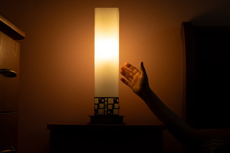 Female hand holding night light on bedside table in cozy bedroom with warm light near bed, bedroom lightingの写真素材