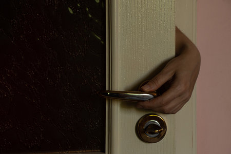Female hand opening bedroom door handle in dark room in apartment, invasion, break-in, fear and danger themeの写真素材