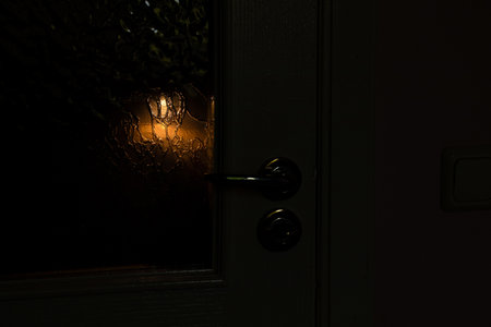 Light is visible on the glass of the door behind the door in the dark in the apartment at night, breaking and entering into the apartmentの写真素材