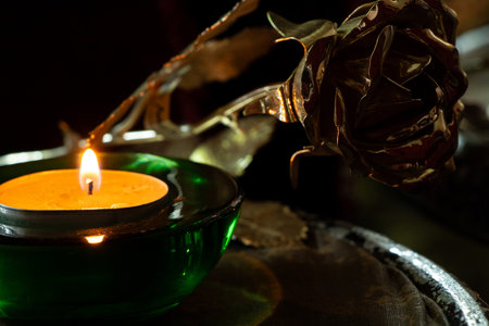 Golden rose and burning candle in green candlestick on chair near mirror in dark roomの写真素材