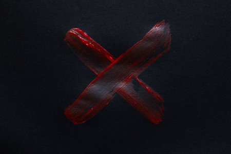 Red watercolor cross painted with brush on black paper close upの写真素材