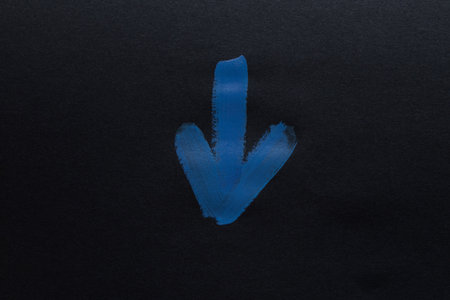 Blue painted arrow pointing down on black paper close up