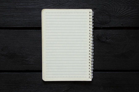 Open lined spiral notebook lies on black wooden background and top view, template for notes