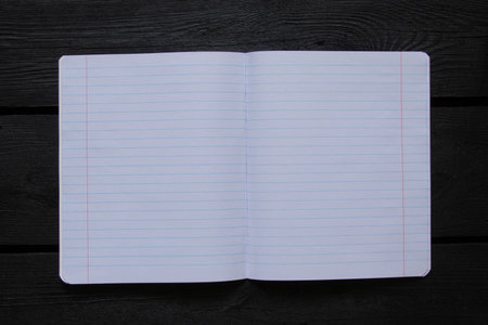 Open school notebook lined on black wooden table and top view, blank pages for notes, used as...