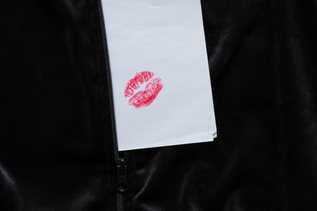Bright lip print with red lipstick on white paper on black fabric close-up, symbol of kiss and...