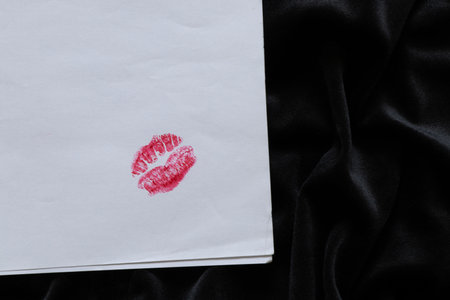 Bright lip print with red lipstick on white paper on black fabric close-up, symbol of kiss and romance, love and messageの写真素材