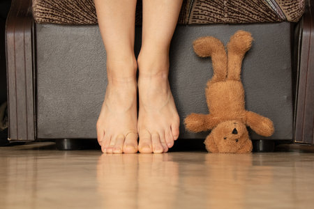 Teddy bear standing on head near woman bare feet, home scene, baby toy near bare feet on floor, funny and cozy momentの写真素材