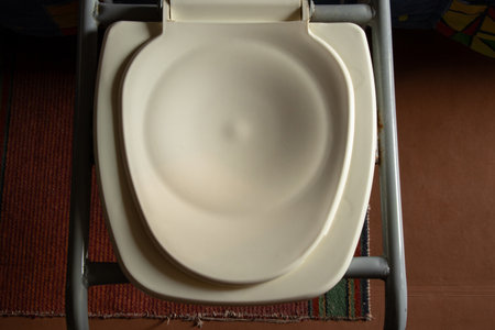 Portable toilet for people with limited mobility in an old apartment, plastic seat with a bucket,...