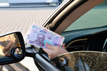 A woman's hand holds out hryvnia bills from a car window, money in a car, cash in hand